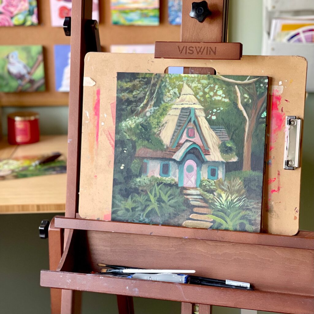 a photo of a partially finishes painting on an easel, of a colorful cottage in the woods.